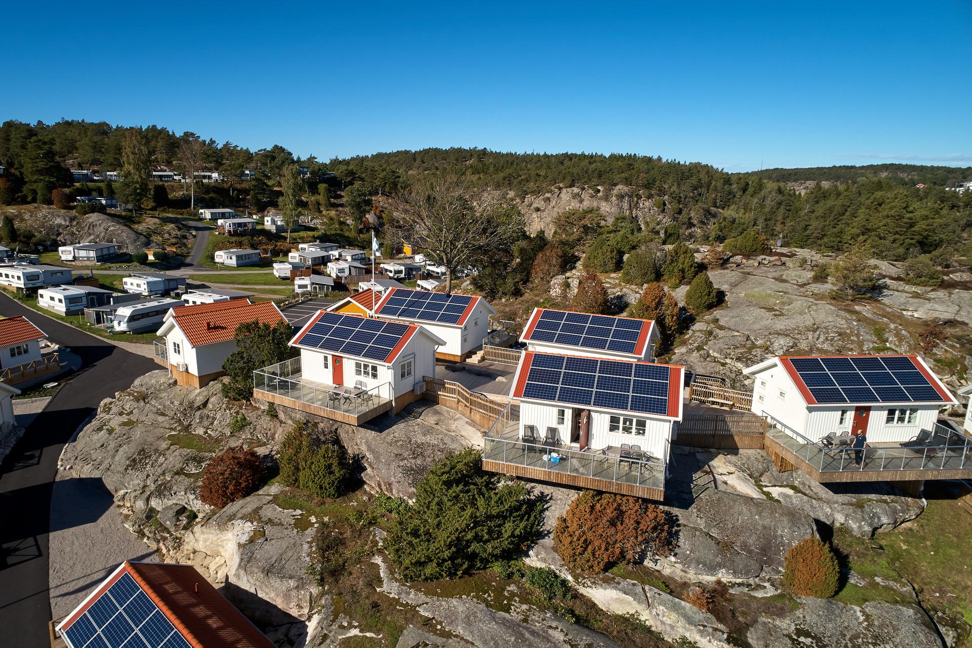Kleine huisjes met zonnepanelen op hun dak links, caravans rechts. Ze staan op rotsachtige kliffen. Bos op de achtergrond.